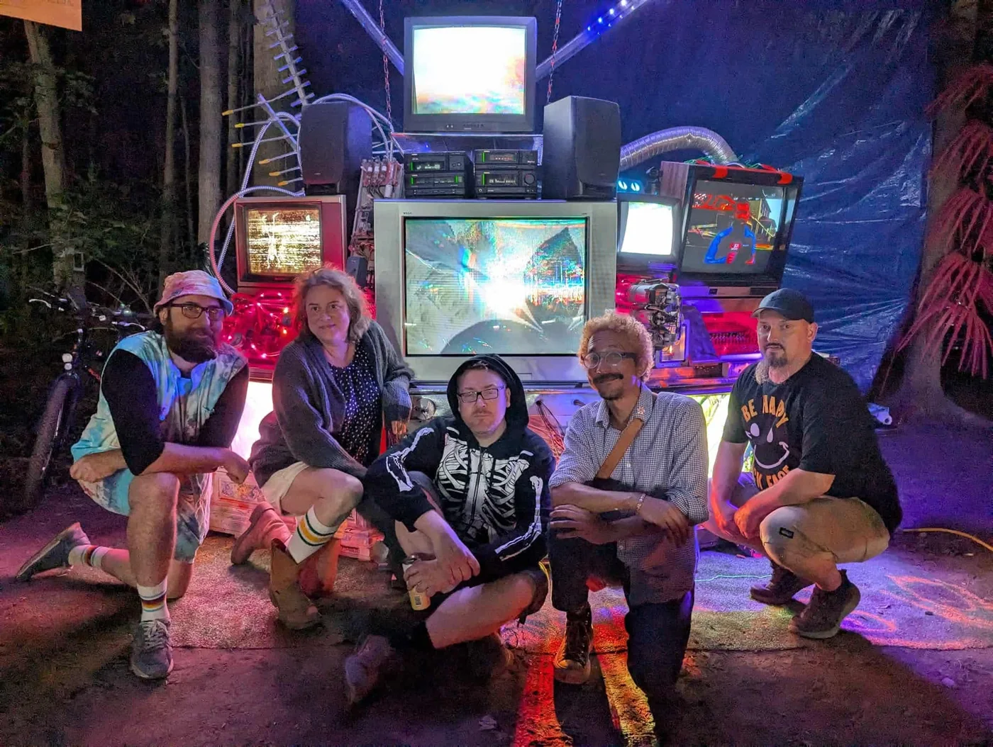 A group gathered in front of The Technostalgic Escape Pod’s stacked analog televisions and colorful screens.